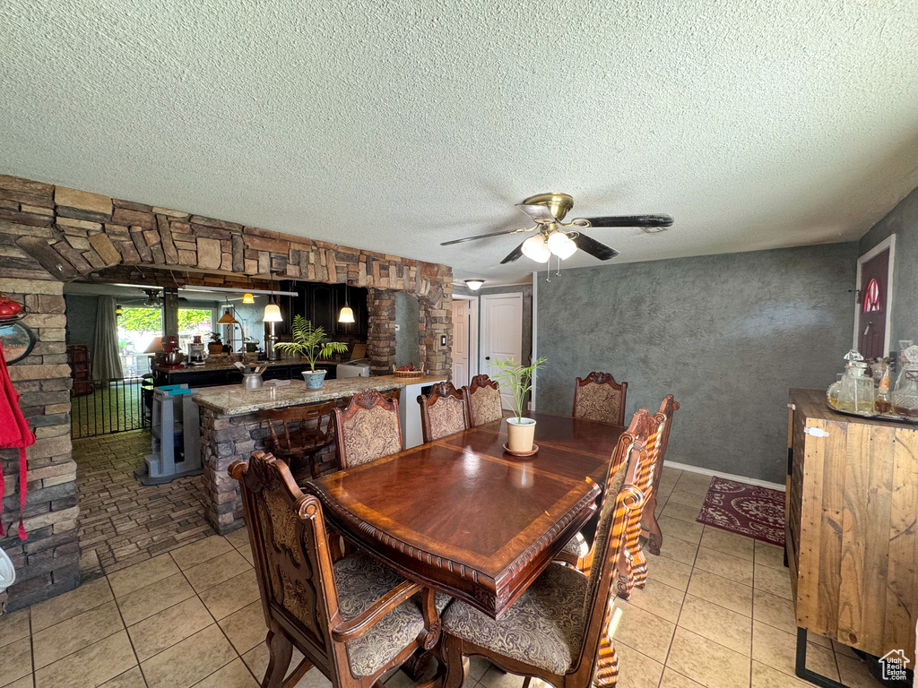 Dining room with a textured ceiling, a ceiling fan, light tile patterned flooring, and bar area