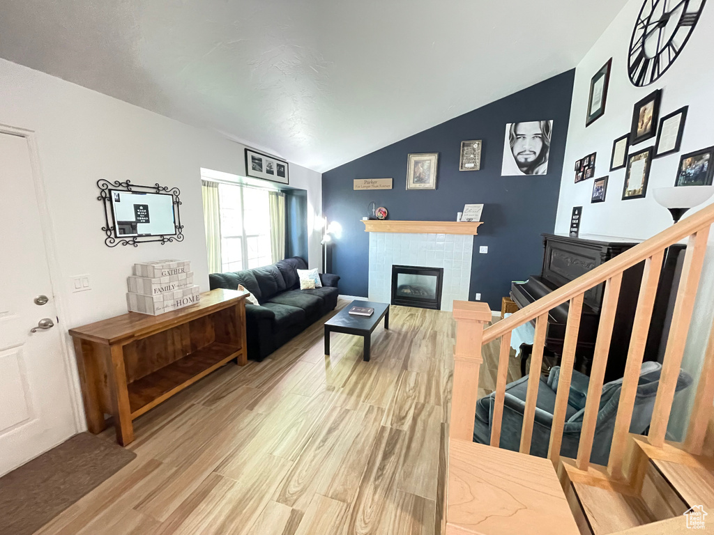 Living area featuring light wood-style floors, a fireplace, vaulted ceiling, and stairway