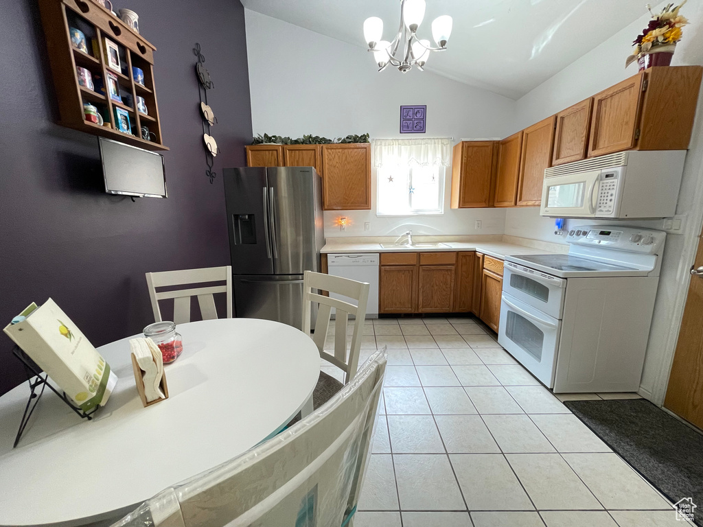 Kitchen with white appliances, brown cabinets, vaulted ceiling, light countertops, and light tile patterned floors