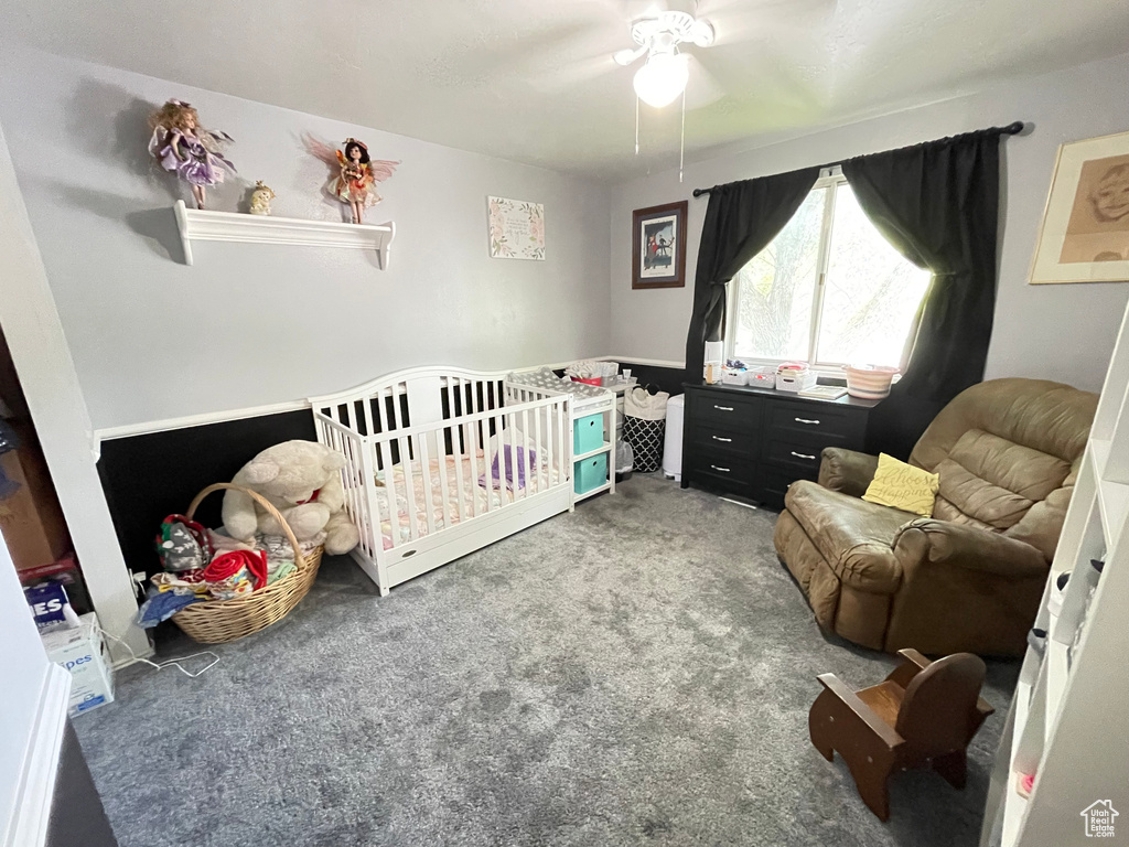 Carpeted bedroom featuring a nursery area and a ceiling fan