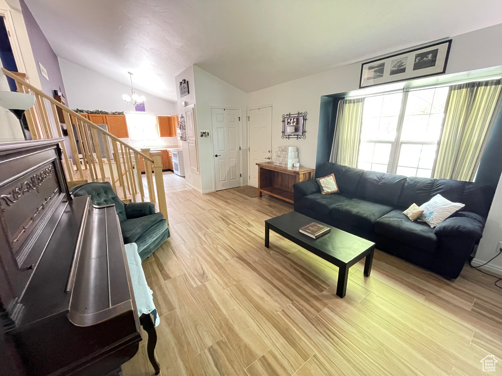 Living room with a chandelier, lofted ceiling, light wood-style floors, and stairs