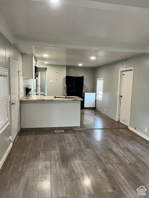 Kitchen with a peninsula, dark wood-style floors, black appliances, baseboards, and white cabinetry