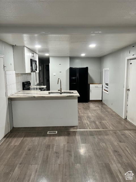 Kitchen featuring black appliances, a peninsula, wood finished floors, and a sink