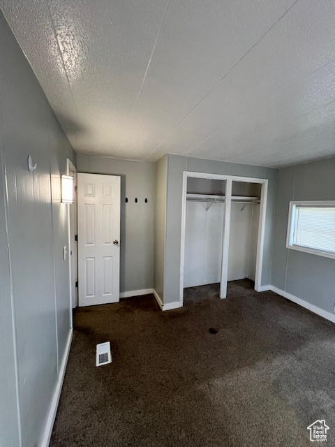 Unfurnished bedroom featuring a textured ceiling, carpet, baseboards, and a closet