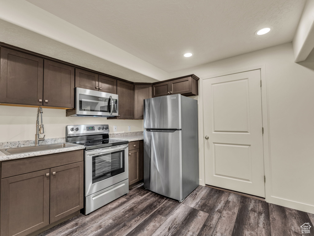 Kitchen with appliances with stainless steel finishes, a sink, dark brown cabinetry, light countertops, and dark wood-type flooring