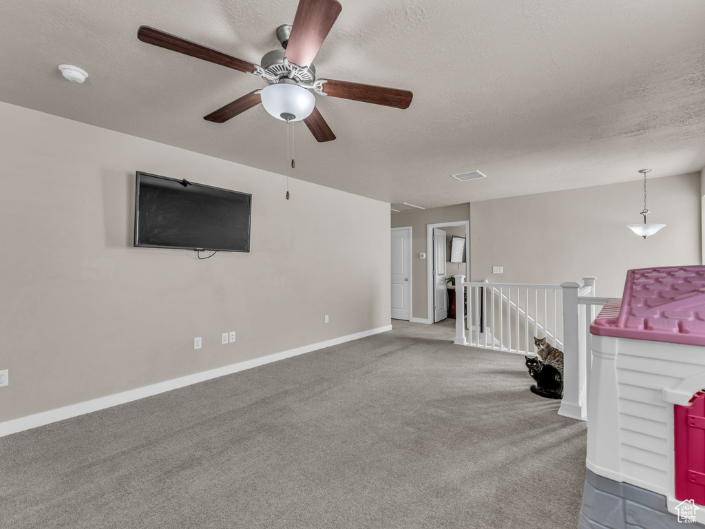 Unfurnished living room featuring ceiling fan, carpet floors, baseboards, and a textured ceiling
