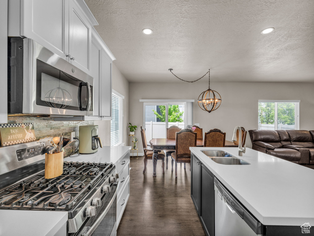 Kitchen with appliances with stainless steel finishes, a sink, a textured ceiling, healthy amount of natural light, and dark wood-style floors