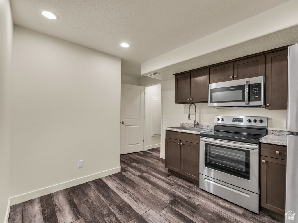 Kitchen featuring appliances with stainless steel finishes, a sink, dark brown cabinets, dark wood-style flooring, and recessed lighting