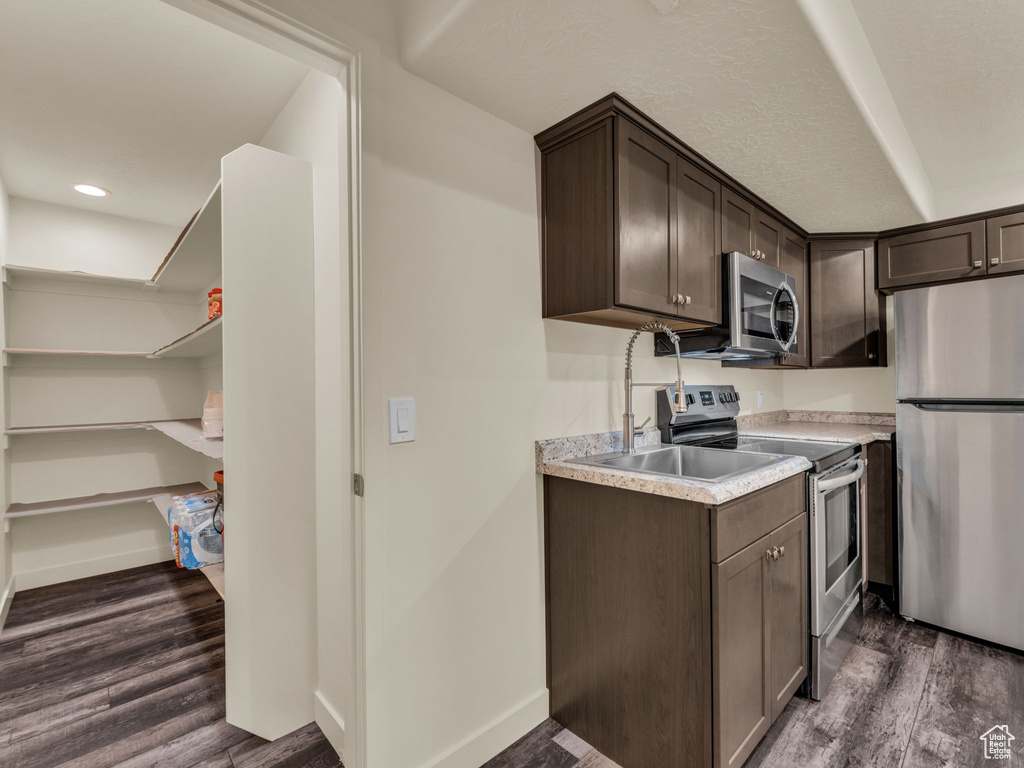 Kitchen with stainless steel appliances, dark brown cabinets, light countertops, dark wood-style floors, and recessed lighting