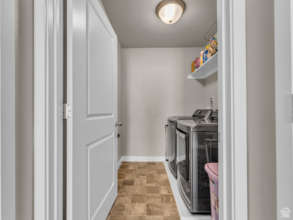 Laundry room featuring washer and clothes dryer, baseboards, a textured ceiling, and stone finish flooring