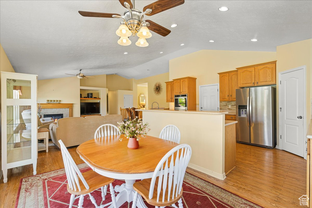 Dining area featuring ceiling fan, lofted ceiling, light wood finished floors, a glass covered fireplace, and recessed lighting