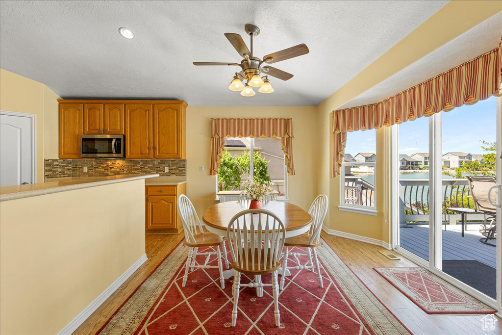 Dining room with light wood-type flooring, baseboards, a ceiling fan, and a textured ceiling