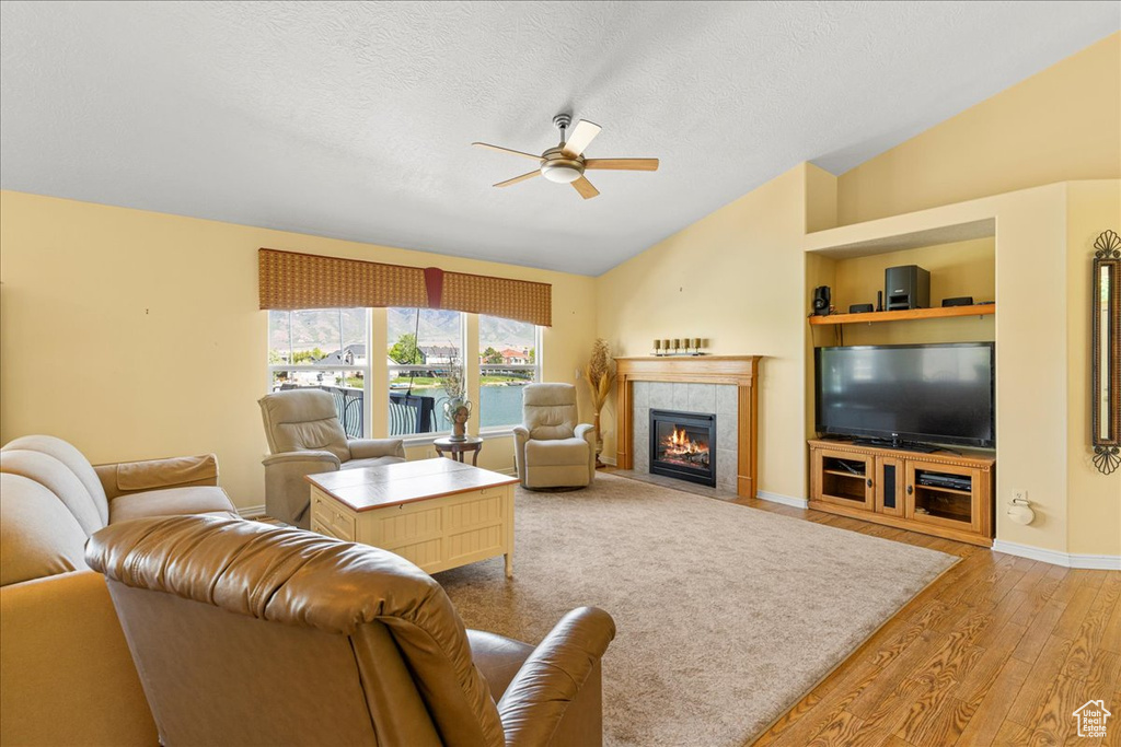 Living area featuring vaulted ceiling, a ceiling fan, light wood finished floors, a tile fireplace, and a textured ceiling