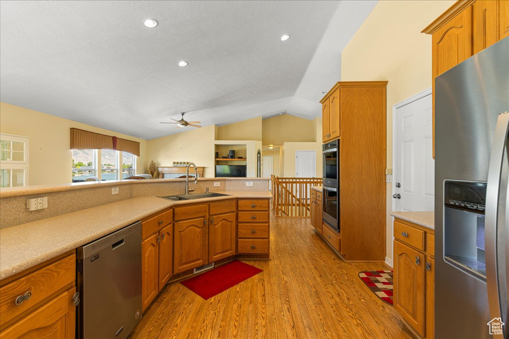 Kitchen featuring appliances with stainless steel finishes, a sink, light wood finished floors, ceiling fan, and lofted ceiling