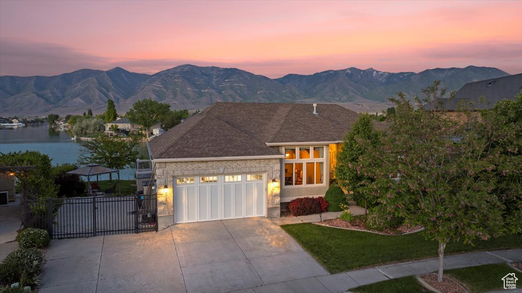 View of front facade featuring an attached garage, concrete driveway, a gate, a water and mountain view, and a shingled roof