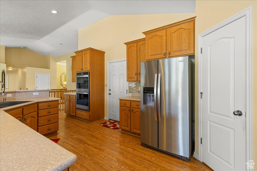 Kitchen with stainless steel appliances, vaulted ceiling, backsplash, light wood finished floors, and light countertops