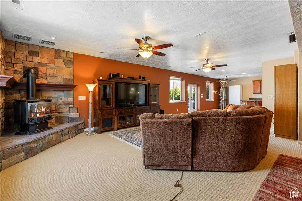 Living room featuring carpet, a ceiling fan, a textured ceiling, a wood stove, and baseboards