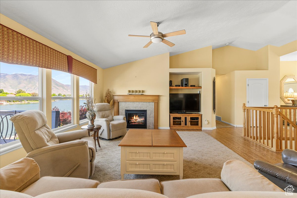 Living room with a ceiling fan, vaulted ceiling, a tiled fireplace, and wood finished floors