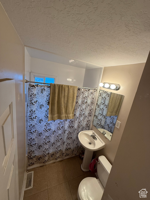Full bathroom featuring tile patterned flooring, toilet, a textured ceiling, a shower with shower curtain, and a sink