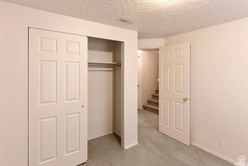 Unfurnished bedroom featuring light carpet, a closet, baseboards, and a textured ceiling