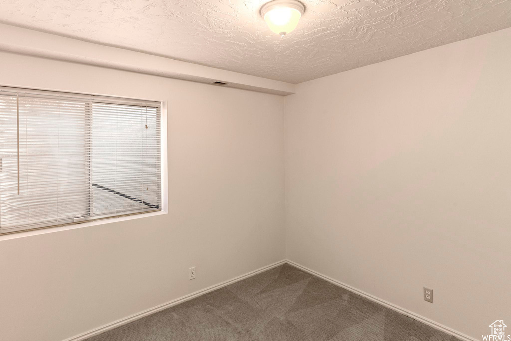 Empty room with a textured ceiling, dark carpet, and baseboards