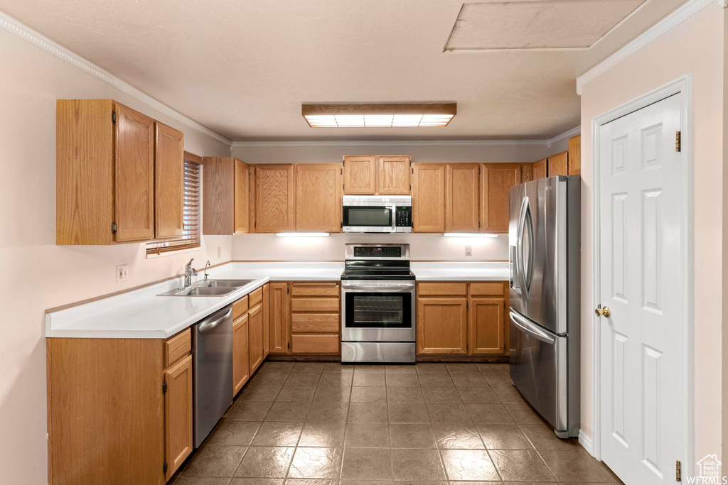 Kitchen featuring appliances with stainless steel finishes, a sink, ornamental molding, light countertops, and tile patterned floors