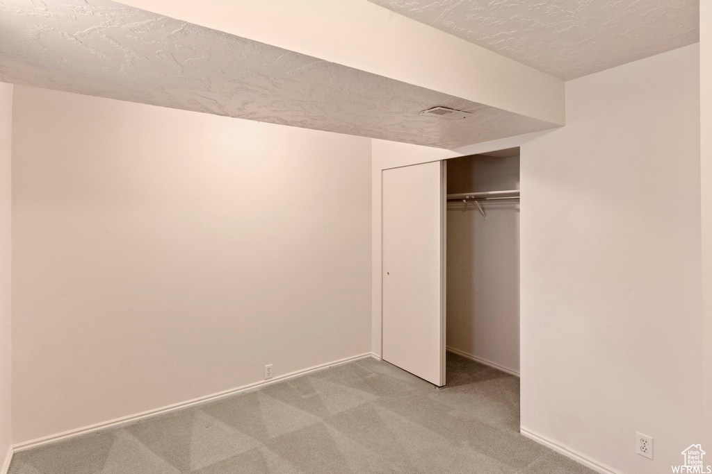 Unfurnished bedroom featuring light colored carpet, baseboards, a closet, and a textured ceiling