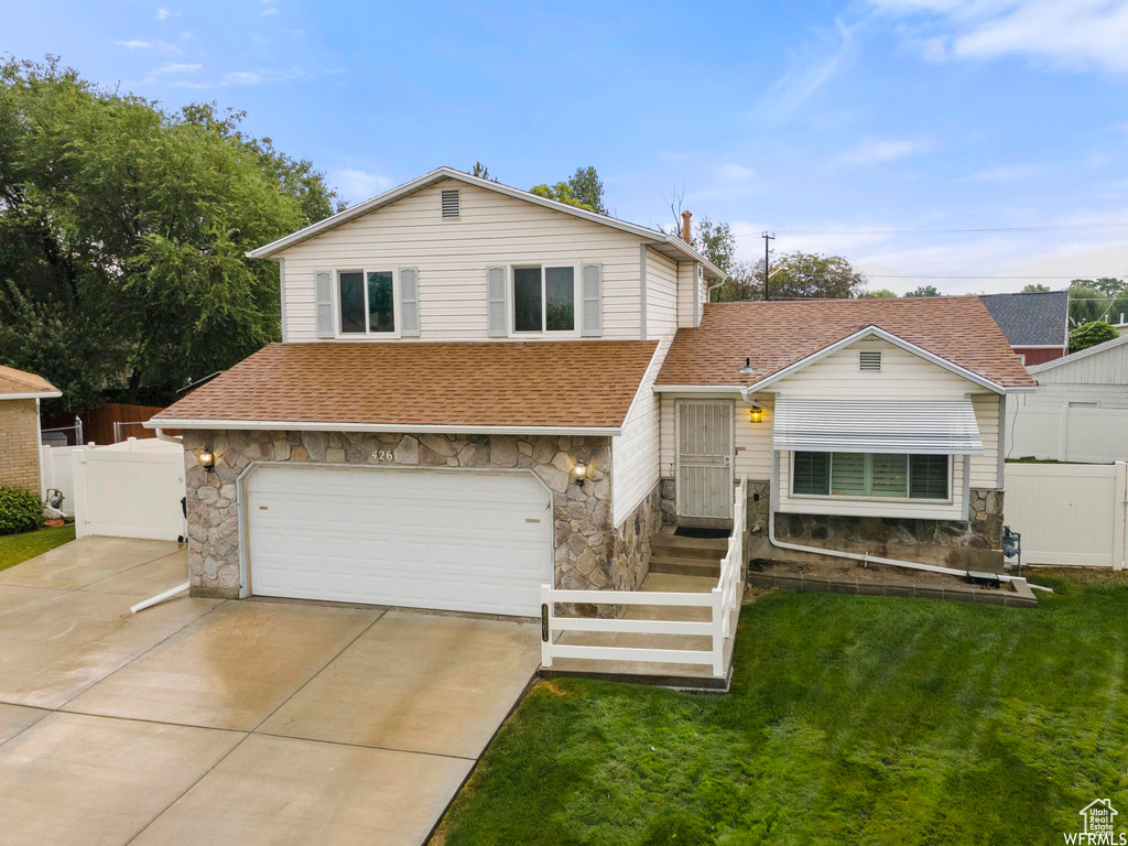 Tri-level home featuring stone siding, a shingled roof, a garage, and concrete driveway