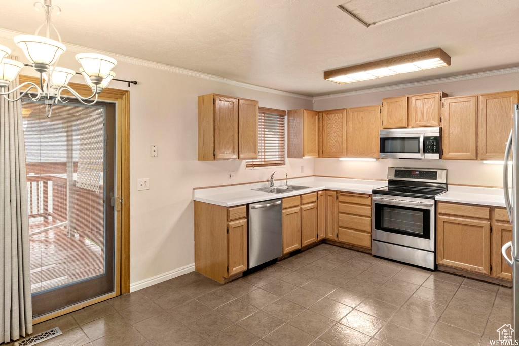 Kitchen with appliances with stainless steel finishes, light brown cabinetry, ornamental molding, light countertops, and a sink