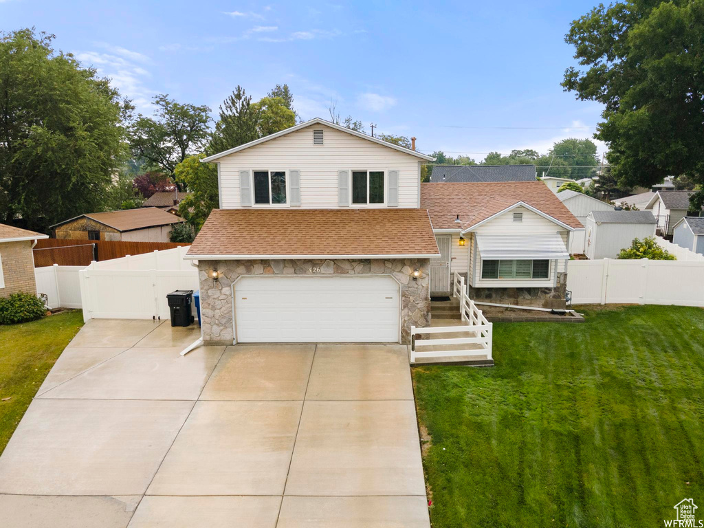 Split level home featuring stone siding, a shingled roof, a garage, driveway, and a gate