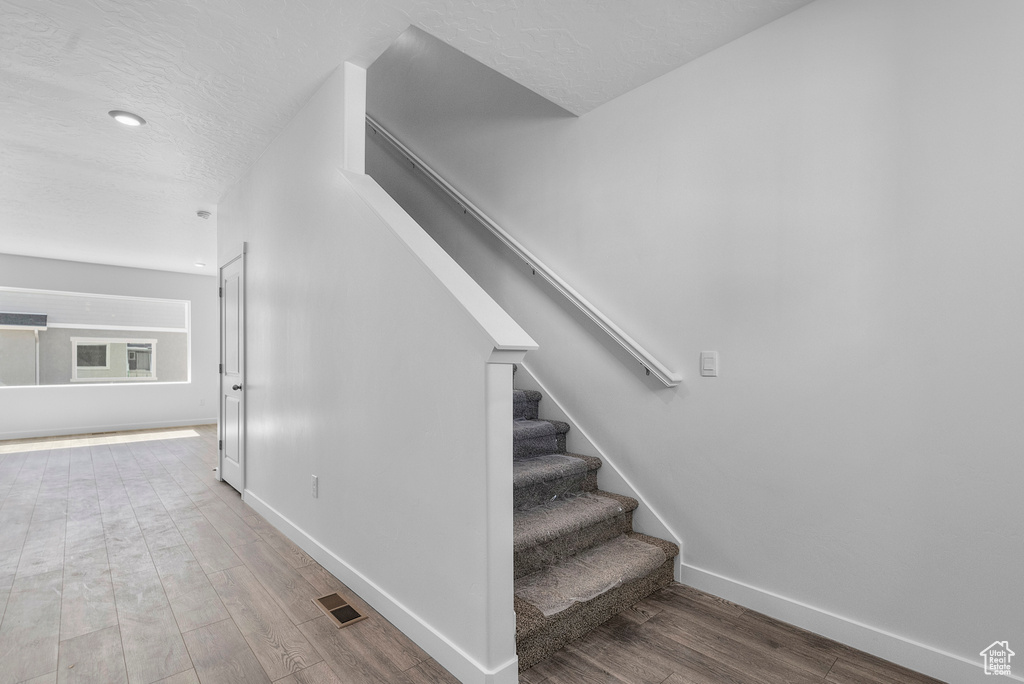 Stairs with baseboards, wood finished floors, recessed lighting, and a textured ceiling