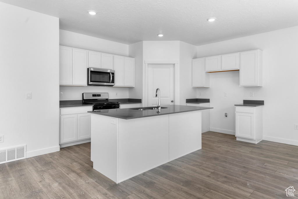 Kitchen featuring appliances with stainless steel finishes, a sink, dark countertops, white cabinets, and recessed lighting