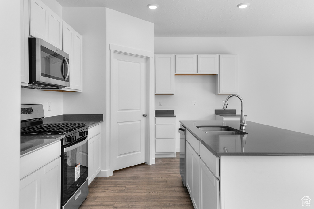 Kitchen with appliances with stainless steel finishes, a sink, dark countertops, a kitchen island with sink, and recessed lighting