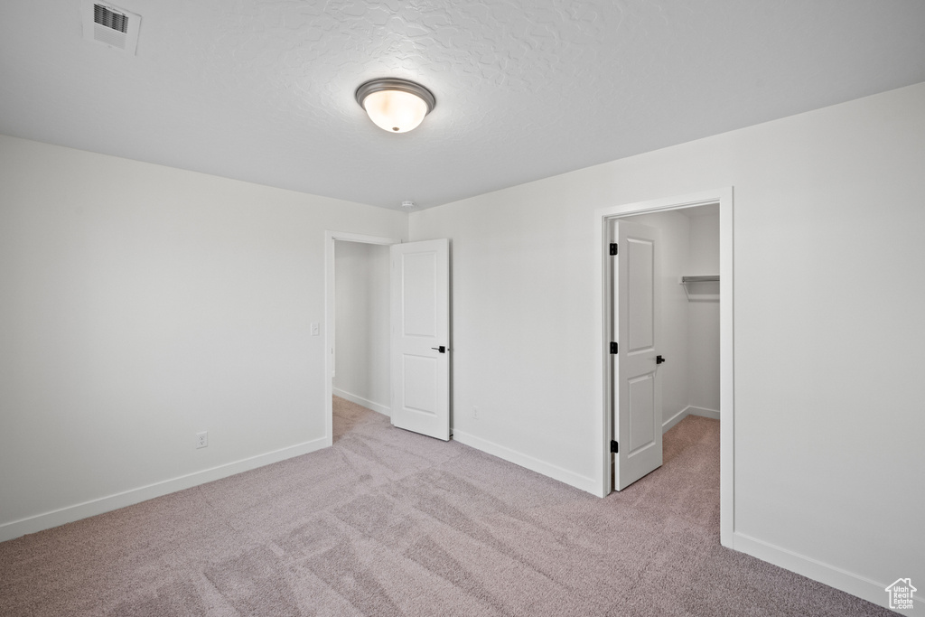 Unfurnished bedroom featuring light colored carpet, baseboards, a spacious closet, a textured ceiling, and a closet