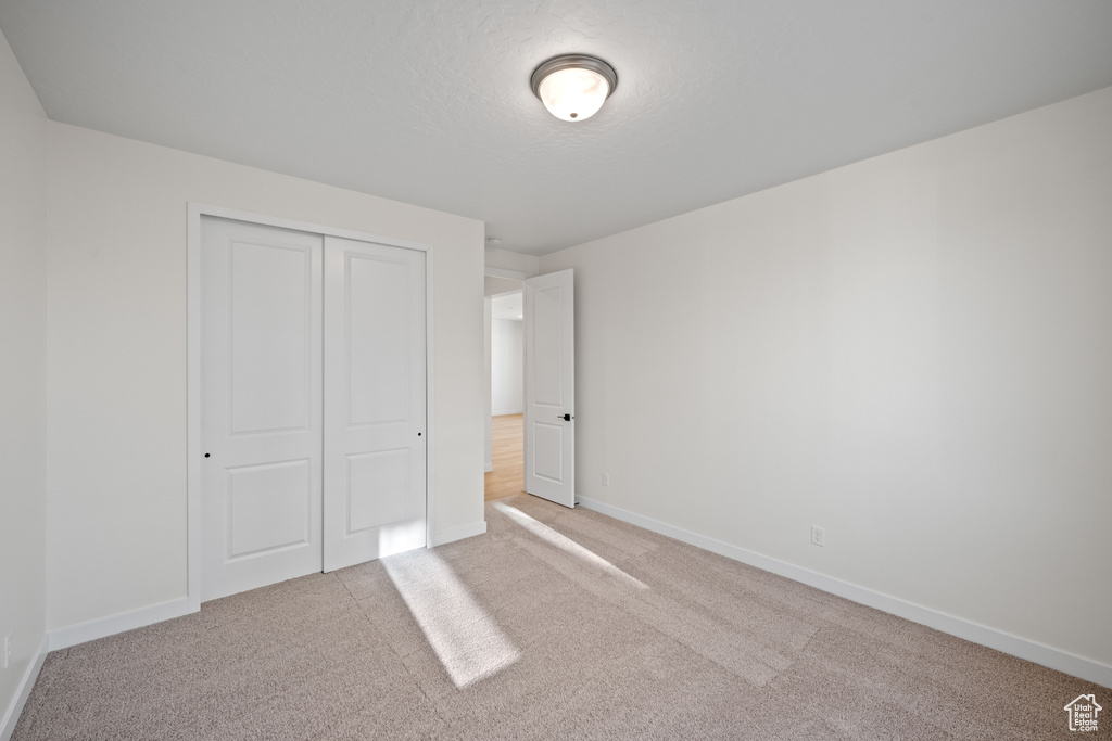 Unfurnished bedroom with baseboards, a closet, and light colored carpet