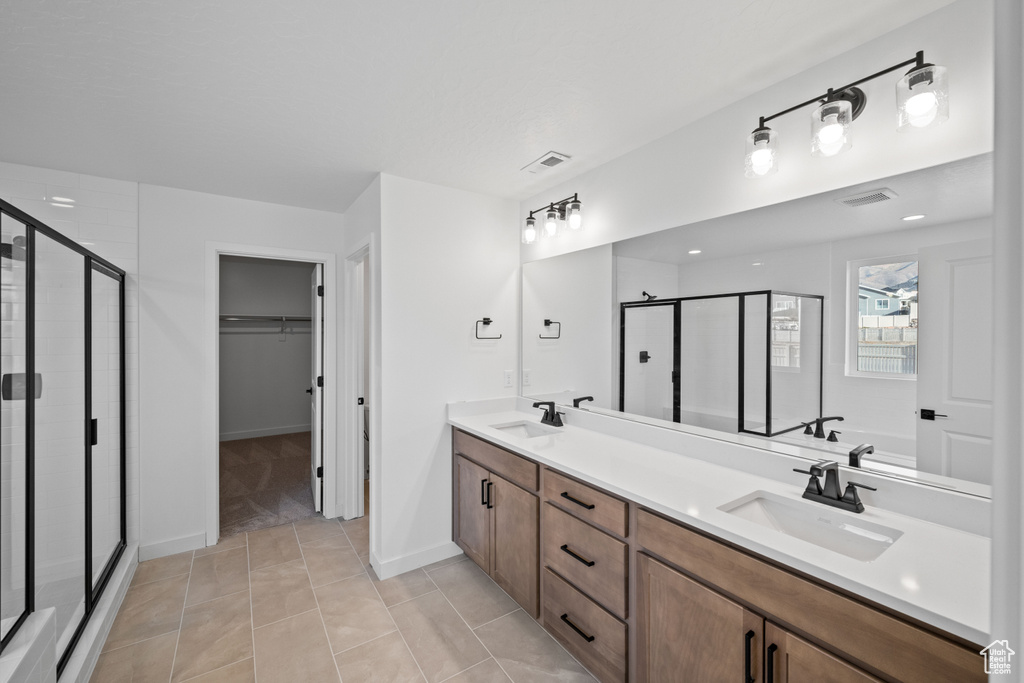 Full bath featuring a shower stall, double vanity, a walk in closet, tile patterned flooring, and baseboards