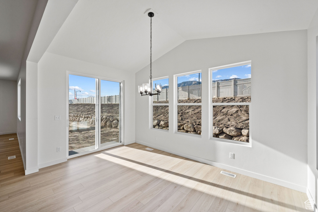 Unfurnished dining area featuring a chandelier, vaulted ceiling, wood finished floors, and baseboards