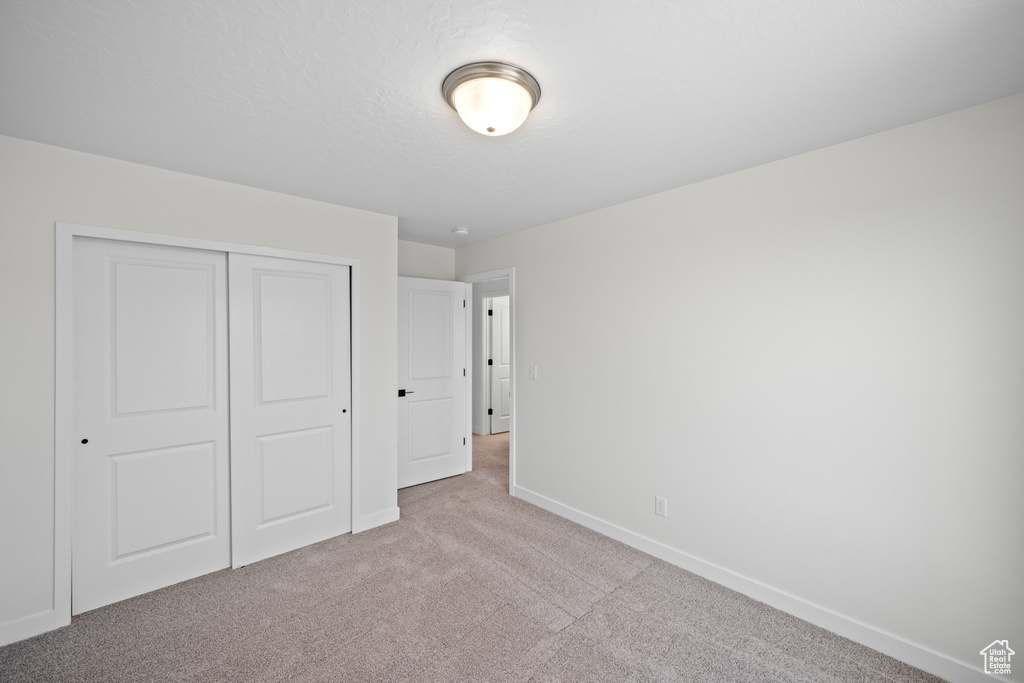 Unfurnished bedroom with light colored carpet, baseboards, and a closet