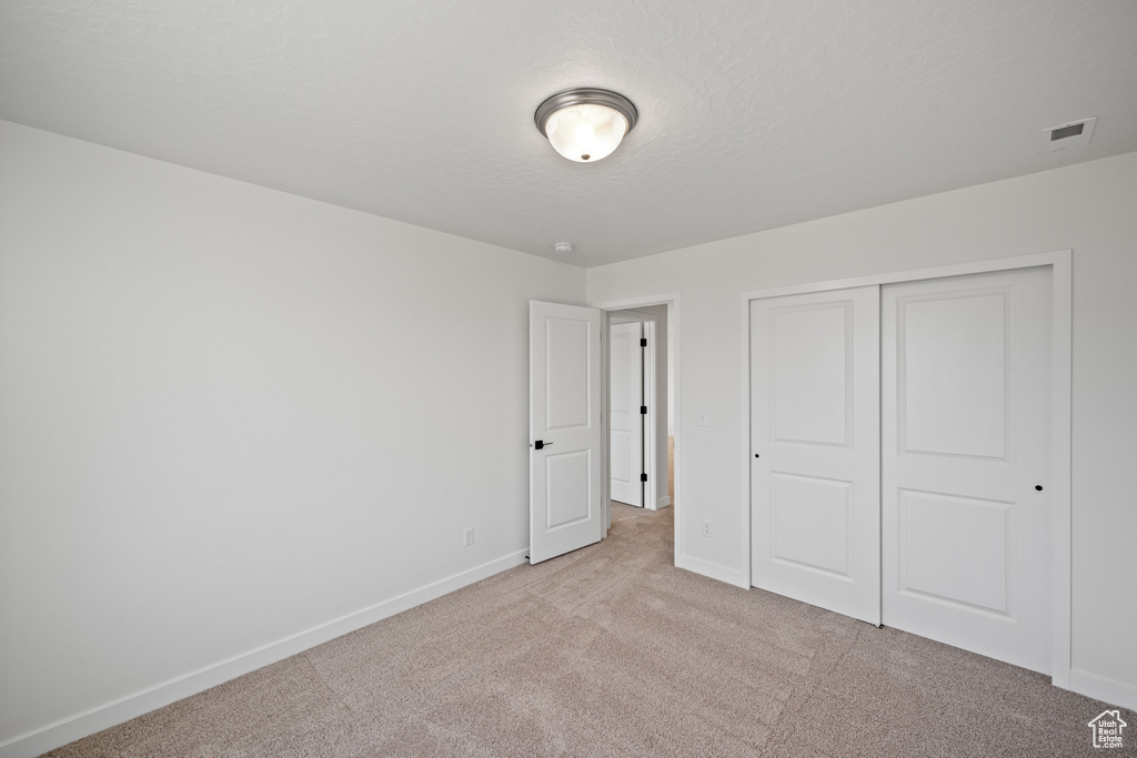 Unfurnished bedroom featuring light carpet, baseboards, and a closet