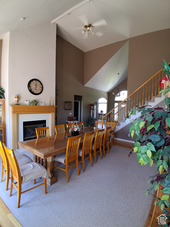 Dining space with high vaulted ceiling, stairs, a glass covered fireplace, carpet floors, and ceiling fan