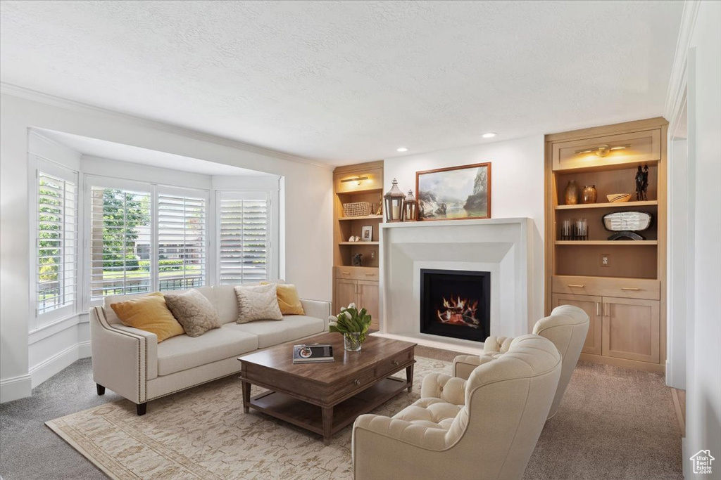 Living room with a warm lit fireplace, built in shelves, light colored carpet, a textured ceiling, and crown molding