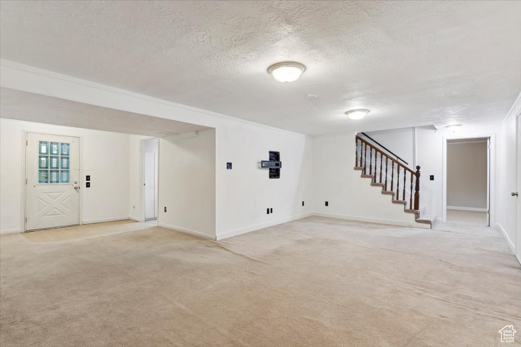 Finished basement featuring light carpet, a textured ceiling, stairway, and baseboards