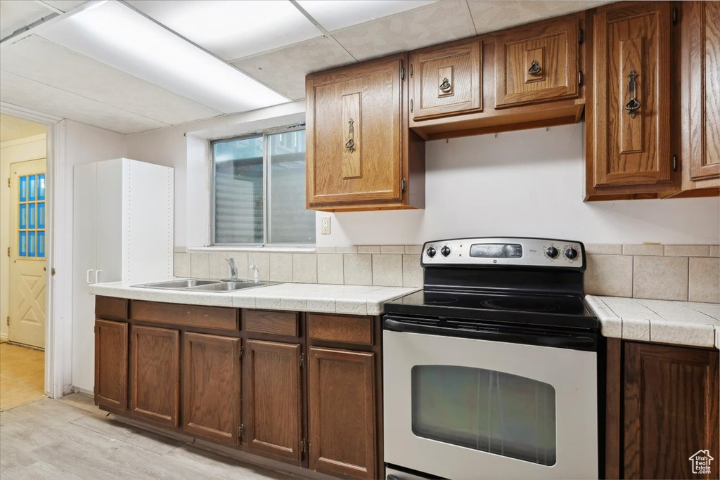 Kitchen with stainless steel range with electric cooktop, a sink, tile countertops, light wood-style floors, and brown cabinets