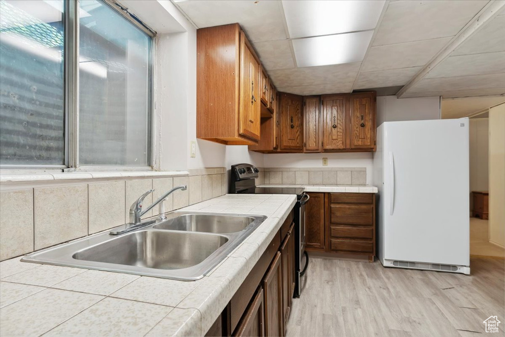 Kitchen with stainless steel range with electric cooktop, tile counters, freestanding refrigerator, a sink, and light wood-type flooring