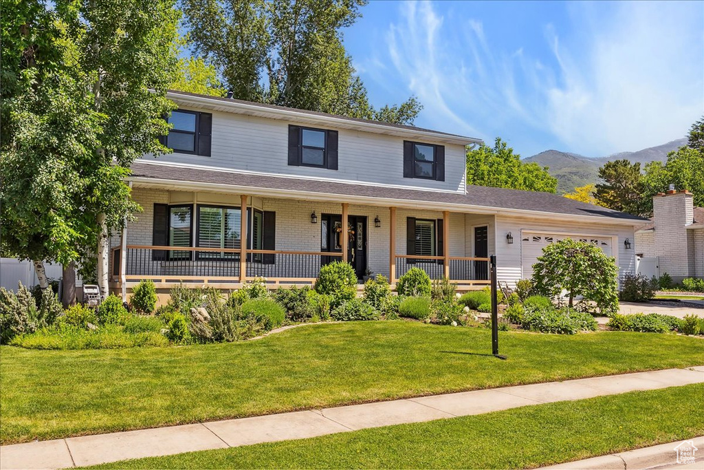 View of front of home featuring a garage, a mountain view, a front yard, covered porch, and brick siding