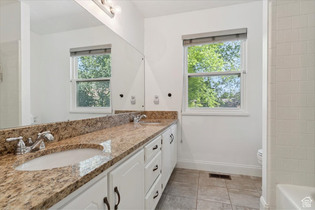 Bathroom with toilet, double vanity, baseboards, a tub, and tile patterned flooring