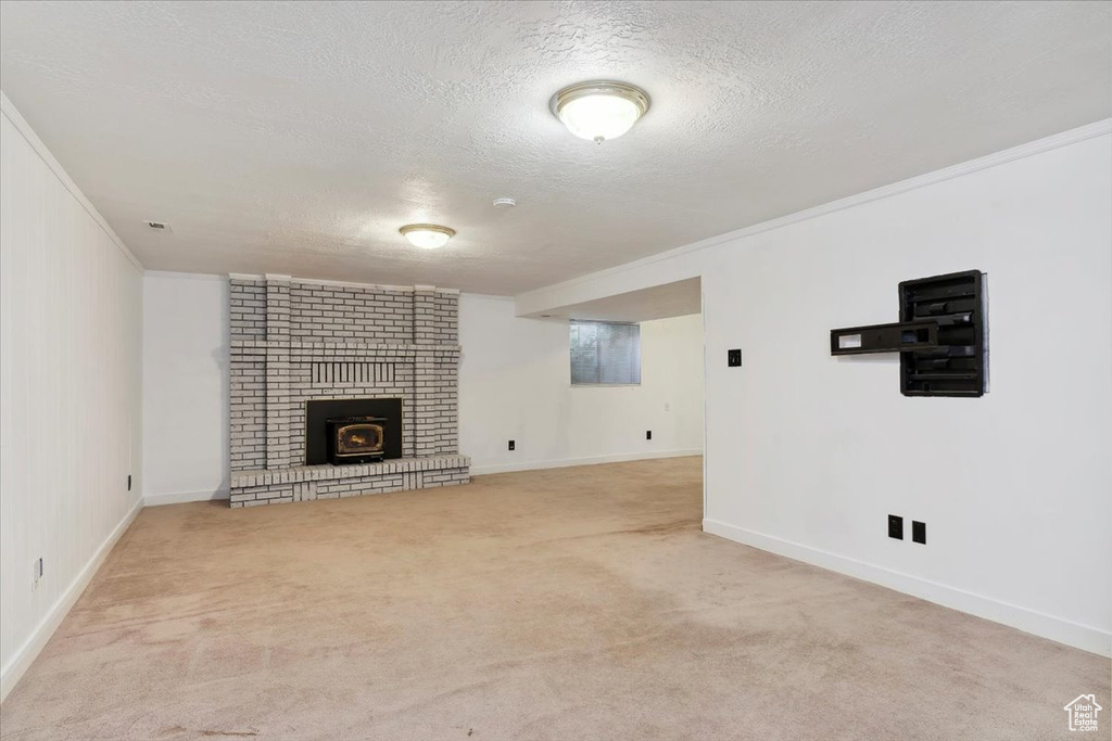 Unfurnished living room featuring carpet flooring, a textured ceiling, ornamental molding, a fireplace, and baseboards