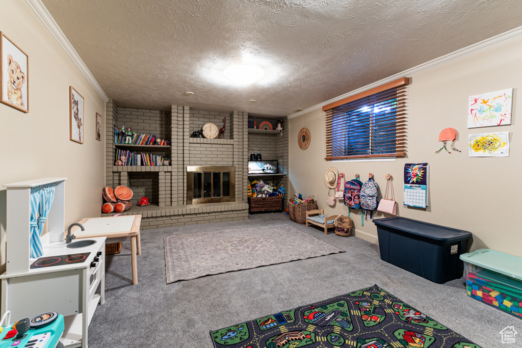 Game room featuring ornamental molding, a textured ceiling, carpet flooring, and a fireplace