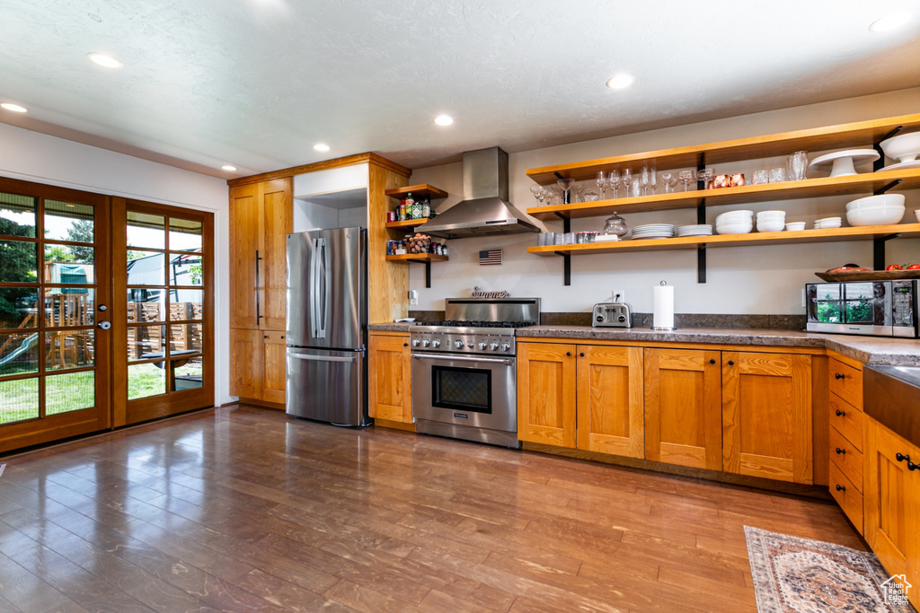 Kitchen featuring appliances with stainless steel finishes, wall chimney range hood, open shelves, wood finished floors, and recessed lighting