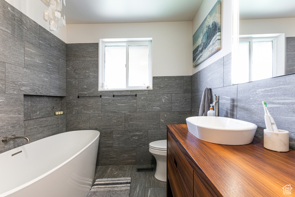 Full bath with tile walls, plenty of natural light, a freestanding tub, vanity, and toilet